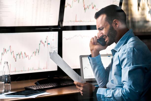 istock Stock Traiding. Trader sitting at office talking on smartphone discussing document with businesspartner concerned 1271432148