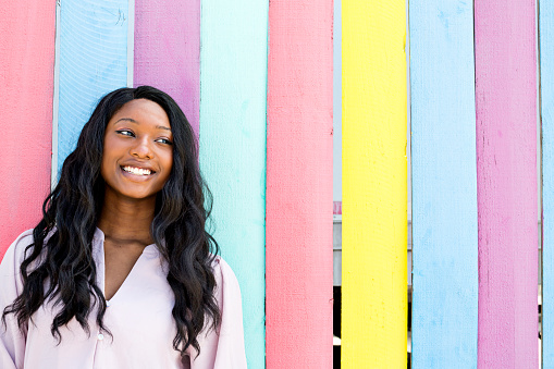 Smiling and beautiful African-American teenager stands in front of brightly colored wall outdoors i