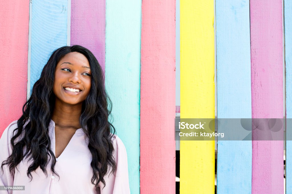 Confident and stunning teen outdoors infront of neon-colored wall Smiling and beautiful African-American teenager stands in front of brightly colored wall outdoors i Multi-Colored Background Stock Photo