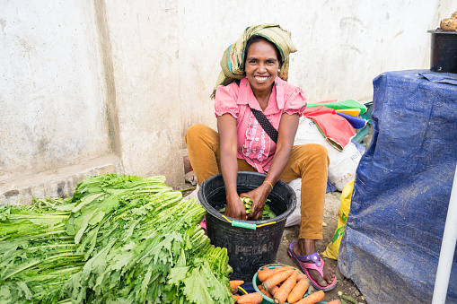 Maubisse / Timor Leste - July 25, 2018: Timorese woman with headscarf and colorful traditional clothes at vegetable stall on the street