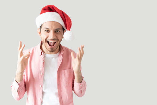 Hispanic man feeling great about Christmas and screaming excited in a studio with grey background