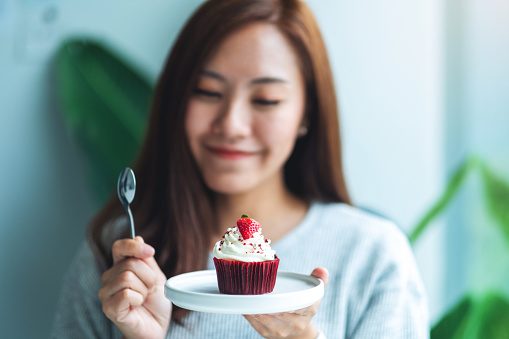A beautiful asian woman holding and eating a red velvet cup cake