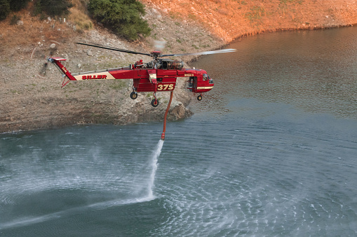 a firefighter emergency helicopter extinguishes a fire and sprays water from a basket over a column of black smoke over a city or wildfire