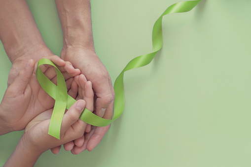 Manos adultas y niños sosteniendo cinta verde de lima sobre fondo verde, niños Conciencia de salud mental y conciencia de linfoma, Día Mundial de la Salud Mental, Día Mundial del Riñón photo