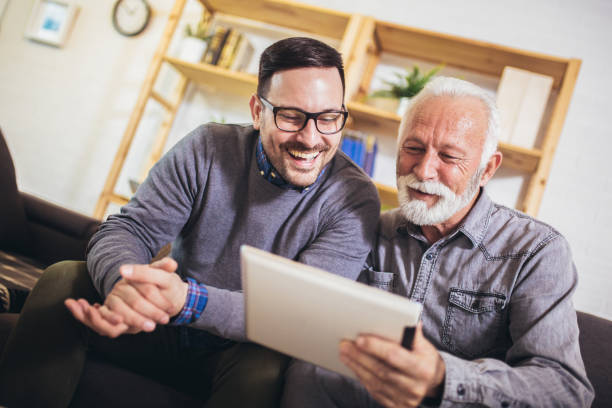 porträt eines älteren mannes mit erwachsenem sohn mit digitalem tablet zu hause - senior adult digital tablet domestic life learning stock-fotos und bilder