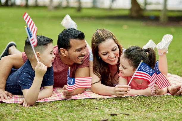 joven familia hispana sonriendo y sosteniendo banderas americanas - fourth of july family flag american flag fotografías e imágenes de stock