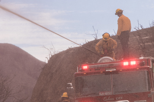 Azusa, California, USA - August 13, 2020: Firefighters fight to contain a wildfire during one of the worst years of the California fire history. At 0% containment, the fire has burned more than 10,000 acres as of Tuesday night with red flag warnings issued due to the windy conditions. Firefighters clear land and throw water during a wildfire in California. The fire has threaten many homes and it has burned down tens of cars and homes. Forcing evacuations all over the county.
