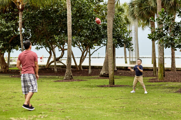 padre ispanico e giovane figlio che giocano a catch al parco pubblico - playing catch foto e immagini stock