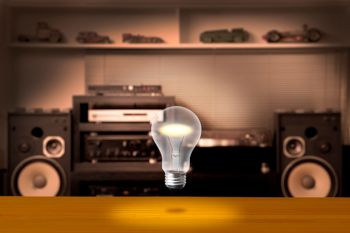 Glowing light bulb in mid-air over the desk against Hi-Fi sound system with copy space.