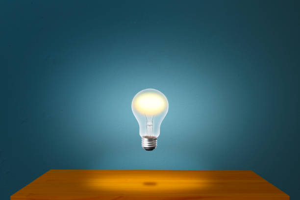 istock Glowing light bulb in mid-air over the desk against blue concrete wall. 1271468511