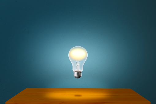Glowing light bulb in mid-air over the desk against blue concrete wall with copy space.