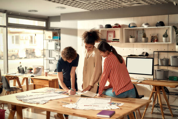 istock Creatives at your service. People making notes, while discussing logo and design of T-shirt. Young man and women working together at custom T-shirt, clothing printing company 1271468603