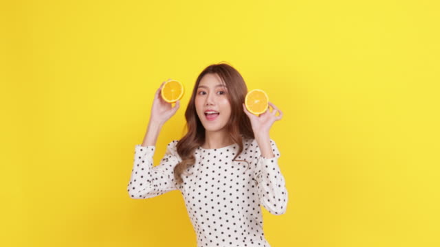 skin care concept. portrait posing asia beauty woman hand touch face and shoulder with yellow background studio shooting.asia female smile happyness holding fresh orange slide