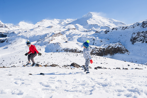 Mixed race kids enjoying outdoors playing with snow having fun at Mt Ruapehu, National Park, New Zealand.