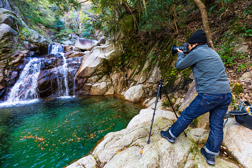 A Japanese photographer taking photos of a waterfall with his camera and tripod near mount Gozaisho in Komono, Mie ken, Japan.