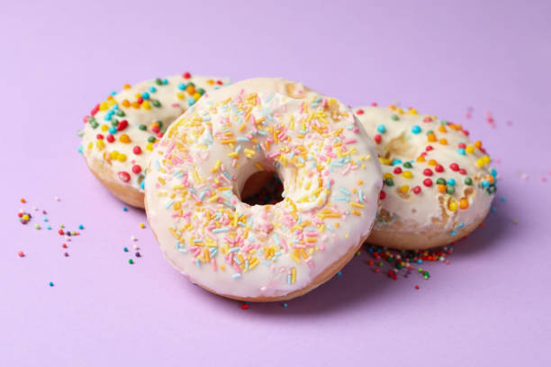 istock Three tasty donuts on violet background, close up 1271472034