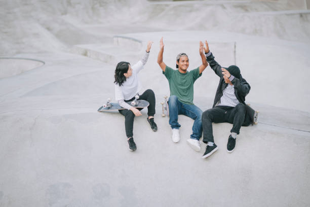 istock Asian skateboarders sitting resting and talking at skateboard park high five 1271473183