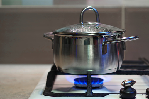A meal is cooked in a stainless steel pan with a glass lid on a gas stove.