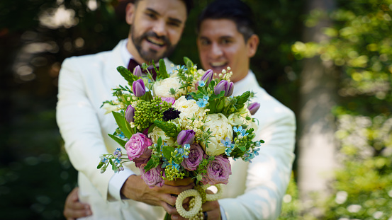 gay bride and groom in white suit with flower bouquet happy together in LBGT wedding ceremony