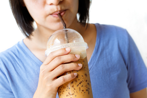 Asian woman drinking ice coffee by straw. Isolated white background.