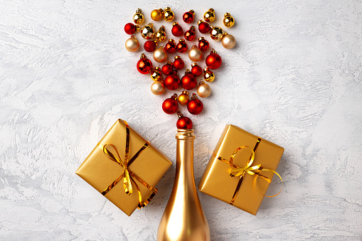 Lots Of Colorful Packed Christmas Gift Boxes Tied With Shining Ribbons And Decoration Items In Wine Glass And Closed Pack Champagne Bottle Neck Wrapped With Golden Paper At Top On Red Background