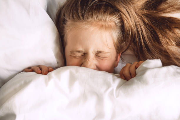 Child hiding under duvet in bed