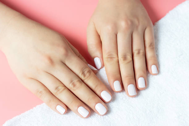 istock Beautiful women's hands with white manicure on pink and white background 1271497156