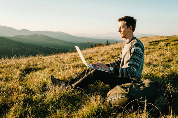 istock Man traveler using laptop computer while enjoying sunset in mountains. Freelancer male working on netbook during vacation holidays in summer. Distant work and travel, freelance as lifestyle concept. 1271497917