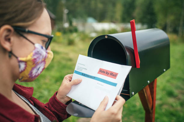Woman in protective face mask sending or receiving letter with voting ballot near a mailbox near her house Woman checking mail during COVID-19 pandemic absentee ballot photos stock pictures, royalty-free photos & images