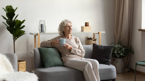 istock Smiling older woman drinking tea, sitting on cozy couch 1271502030