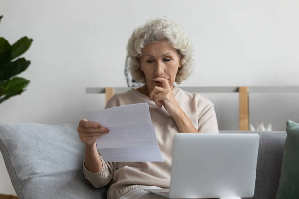 istock Thoughtful mature woman reading letter, using laptop, working with correspondence 1271502075