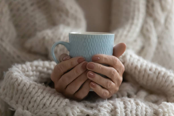 Close up mature woman wrapped warm blanket holding mug Close up mature woman wrapped warm blanket holding mug of coffee or tea, middle aged female enjoying free time, weekend at home, relaxing, drinking hot beverage in morning, starting new day cup of tea hands stock pictures, royalty-free photos & images