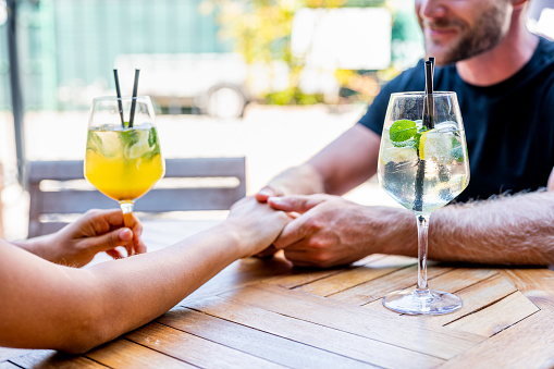 Close up image of holding hand of an unrecognizable caucasian couple, on the wooden table in a bar. Drinks on the table by the hands.