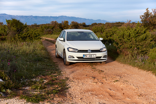 Island Brac / Croatia-05.25.2019: Trip in a Volkswagen Polo from a rental company around the island. The car is standing on a country road among green bushes. On the horizon you can see the mountains