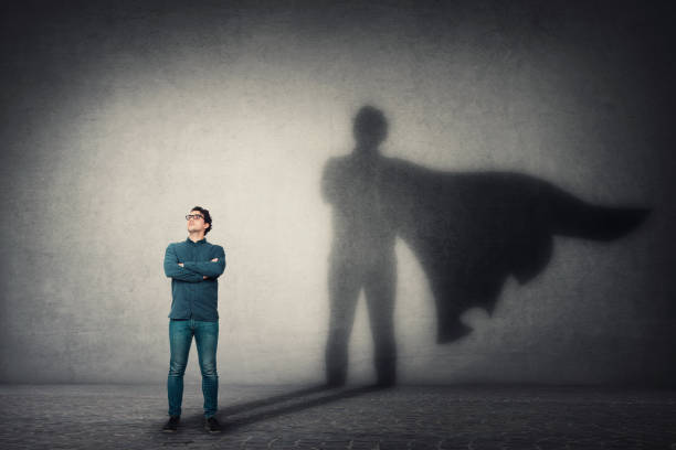 Brave man keeps arms crossed, looks confident, casting a superhero with cape shadow on the wall. Ambition and business success concept. Leadership hero power, motivation and inner strength symbol. Brave man keeps arms crossed, looks confident, casting a superhero with cape shadow on the wall. Ambition and business success concept. Leadership hero power, motivation and inner strength symbol. cape garment photos stock pictures, royalty-free photos & images