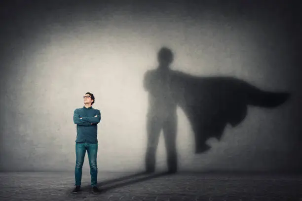 Photo of Brave man keeps arms crossed, looks confident, casting a superhero with cape shadow on the wall. Ambition and business success concept. Leadership hero power, motivation and inner strength symbol.