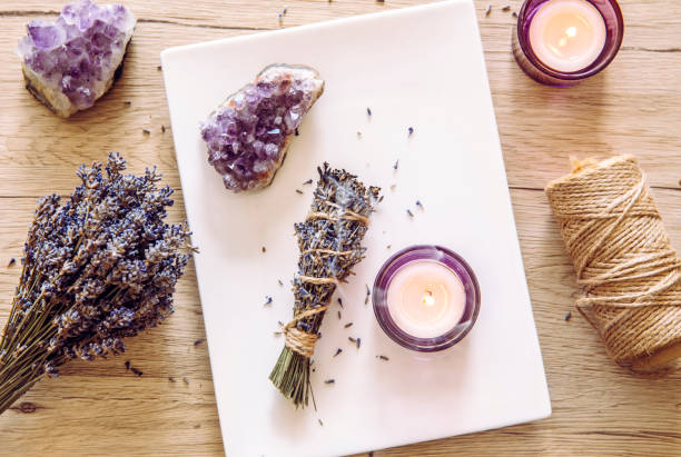 Homemade herbal lavender (lavendula) smudge stick smoldering on white plate with candles and amethyst crystal clusters for decoration. Spiritual home cleansing concept. Homemade herbal lavender (lavendula) smudge stick smoldering on white plate with candles and amethyst crystal clusters for decoration. Spiritual home cleansing concept. crystal stock pictures, royalty-free photos & images