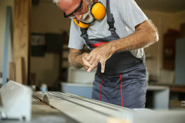 Senior man working as a carpenter in his workshop, injured with a circular saw. About 65 years old, Caucasian male.