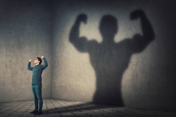 hombre confiado flexionando los músculos imaginar super poder como lanzar una sombra de culturista muscular que muestra bíceps. persona fuerte enfrentando sus miedos. desarrollo personal, fuerza interior, concepto de motivación. - strong shadows fotografías e imágenes de stock