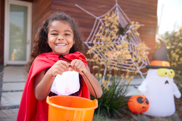 Portrait Of Girl Wearing Fancy Dress Outside House Collecting Candy For Trick Or Treat Portrait Of Girl Wearing Fancy Dress Outside House Collecting Candy For Trick Or Treat trick or treat photos stock pictures, royalty-free photos & images