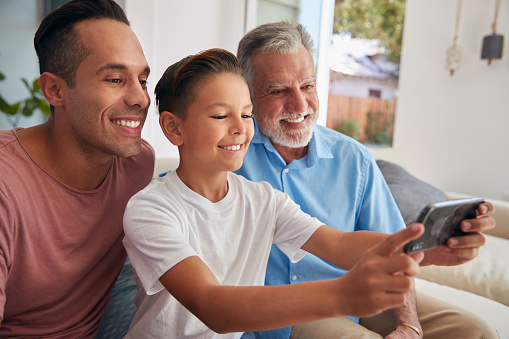 Multi-Generation Male Hispanic Family On Sofa At Home Posing For Selfie On Mobile Phone