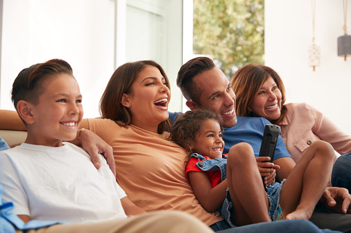 Multi-Generation Hispanic Family Relaxing At Home Sitting On Sofa Watching TV Together