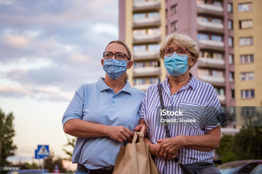 Home caregiver walking senior woman outdoors Outdoor shot of senior woman and female social worker. They are wearing protective face masks, walking in front of apartment in the city. 70-79 Years Stock Photo