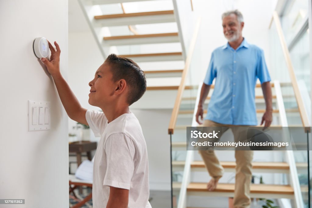 Grandfather With Grandson Adjusting Digital Central Heating Thermostat In Home Thermostat Stock Photo