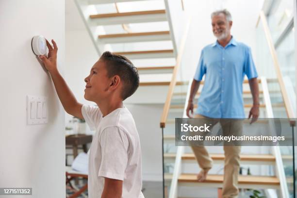 Grandfather With Grandson Adjusting Digital Central Heating Thermostat In Home Stock Photo - Download Image Now