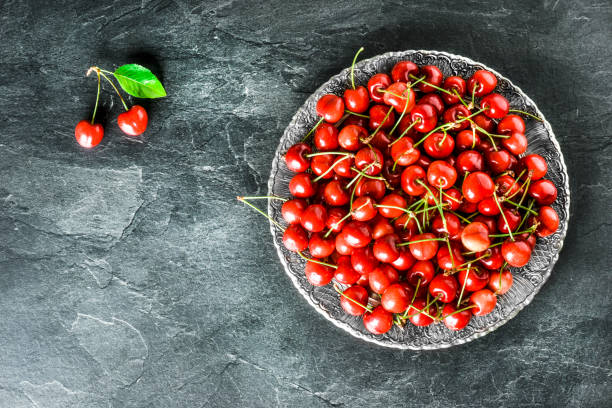 istock Cherries on rustic old silver plate with dark stone background. 1271512110