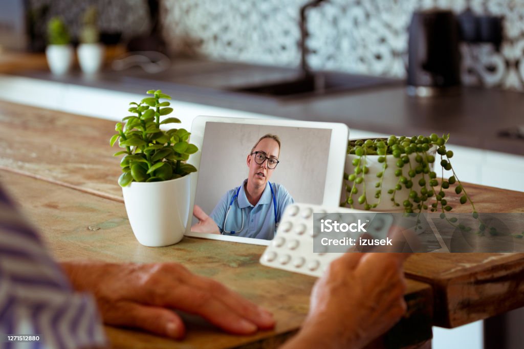 Video call with female doctor during coronavirus pandemic Telemedicine concept. Senior woman using digital tablet and having video call with nurse. Close up of screen and pills. Doctor Stock Photo