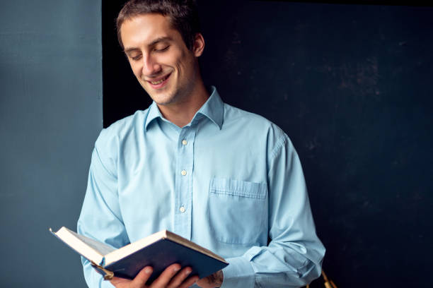 istock young man reading a book, a guy in a blue shirt on a dark blue background. 1271514014