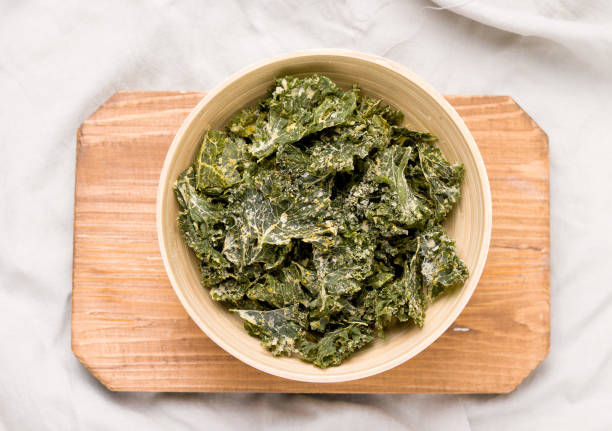 istock Kale chips in bowl on wooden board top view 1271515098