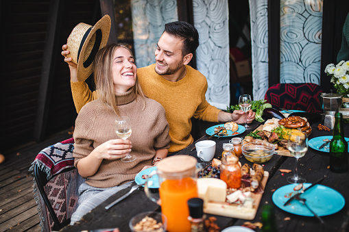 Adorable young modern couple sharing some affectionate during autumn outdoor brunch on a patio in front of log cabin
